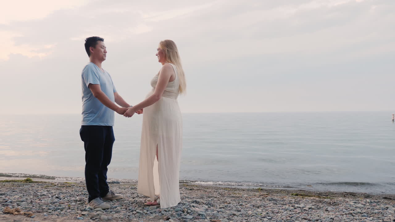 젊은 다민족 부부가 해변에 서 있다 임신한 여자와 아시아 남자 다민족 공동