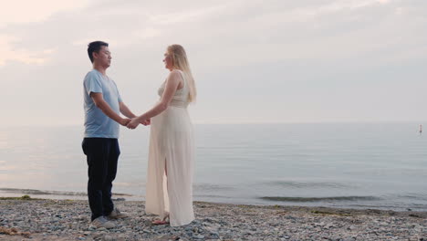 a young multi-ethnic couple stands on the seashore a pregnant woman and an asian man multi-ethnic co