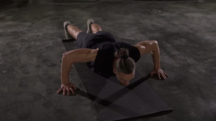 Caucasian man with dreadlocks in black sportswear does push-ups in empty gym or studio. Part of his cross fitness workout body weight training