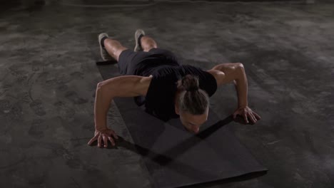 Caucasian-man-with-dreadlocks-in-black-sportswear-does-push-ups-in-empty-gym-or-studio.-Part-of-his-cross-fitness-workout-body-weight-training