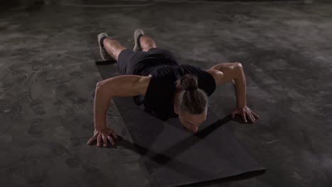 caucasian man with dreadlocks in black sportswear does push-ups in empty gym or studio. part of his cross fitness workout body weight training