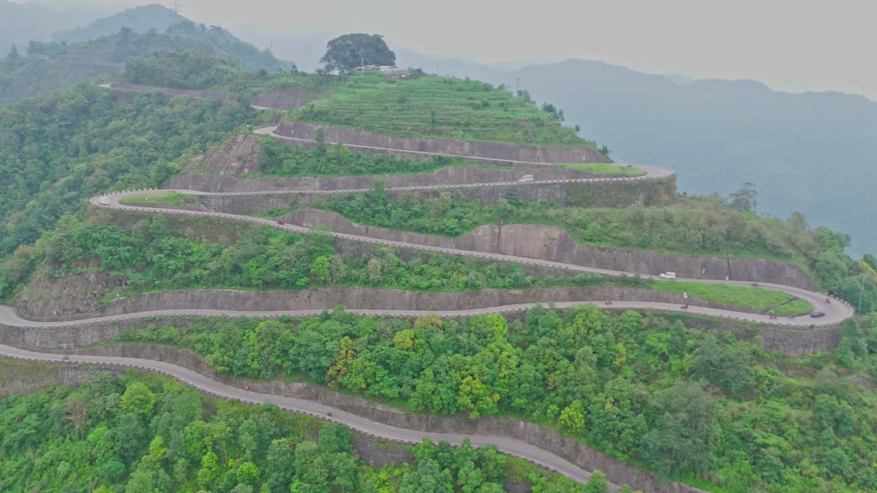 A serpentine road curves gracefully through vibrant green mountains, offering a breathtaking view of natural beauty and human engineering in harmony, captured from a high-altitude aerial perspective.