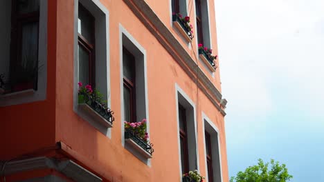 closeup of an old orange building with pink flowers in window boxes