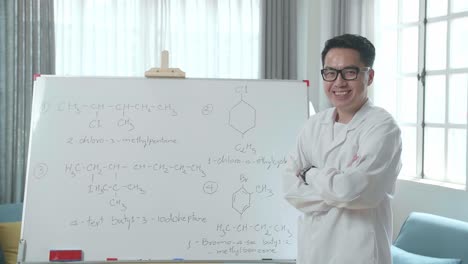 asian male teacher with glasses crossing arms and smiling to camera while teaching chemist at home