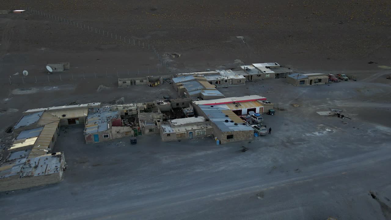 Vista aerea sopra case di un rosso vivido alla base della Laguna Colorada con una chiara vista di scure colline vulcaniche sullo sfondo