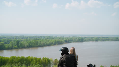 biker hugs girlfriend on green hill top near tranquil lake