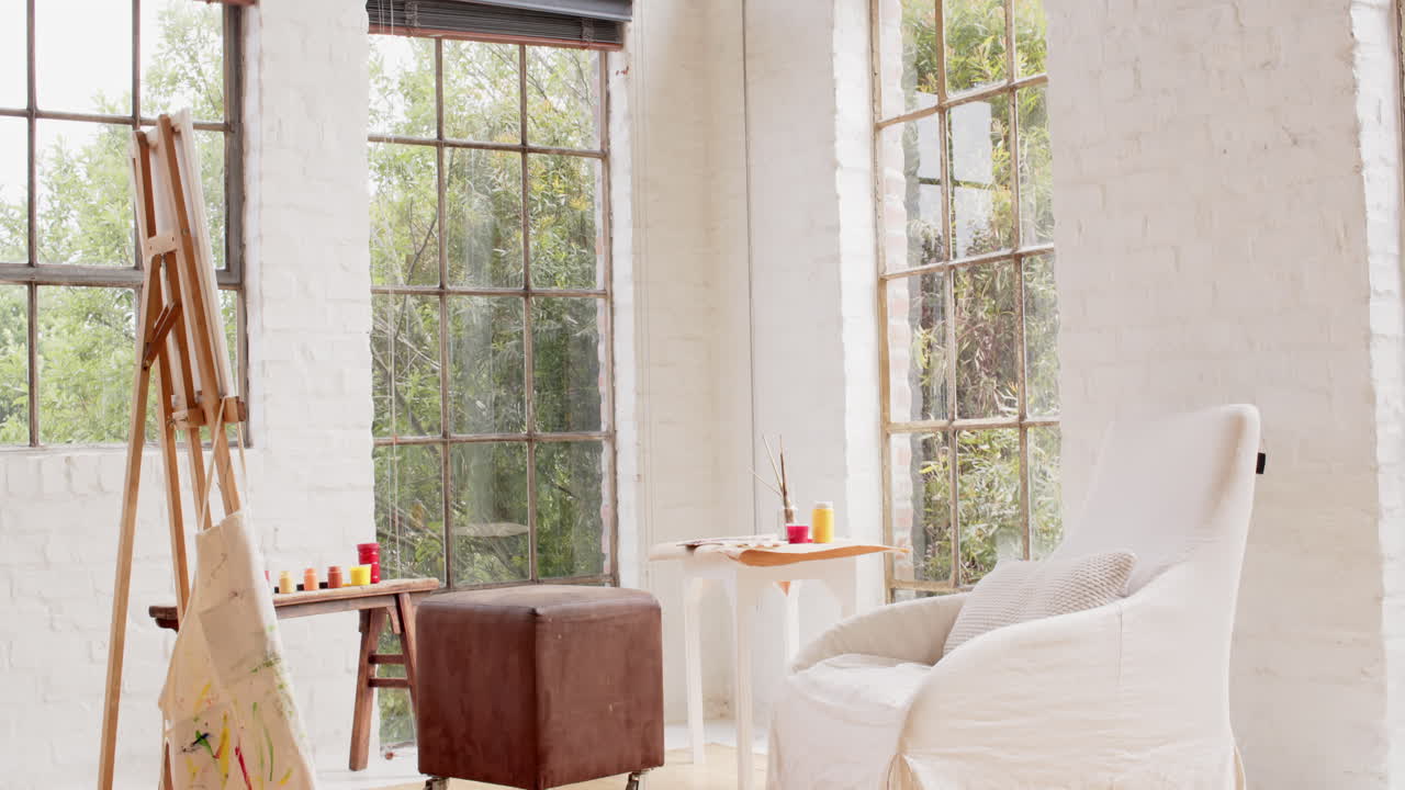 Cozy art studio with easel and chair by large windows, inviting creativity, at home