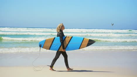 vista lateral de una surfista caucásica senior activa caminando por la playa bajo el sol 4k