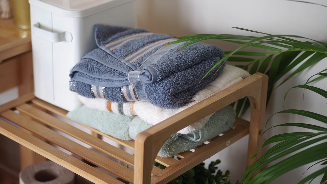 Neatly Folded Towels Stacked on a Wooden Shelf with a Plant