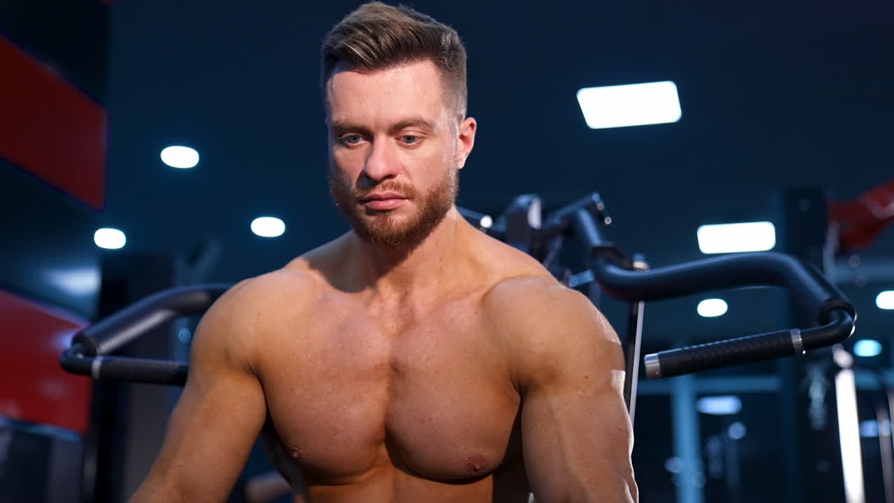 Handsome man with big muscles, posing at the camera in the gym. Modern sport equipment background. Serious bodybuilder.