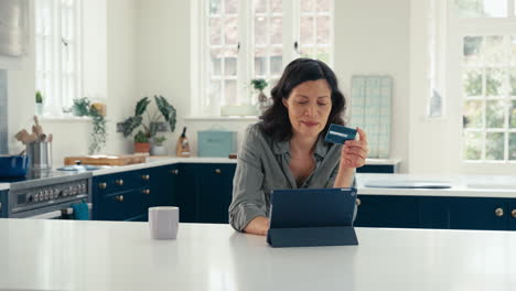 mature woman with credit card using digital tablet at home to book holiday or shop