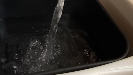 agua de un grifo de mezclador que llena un recipiente de lavado alojado en un fregadero de cerámica