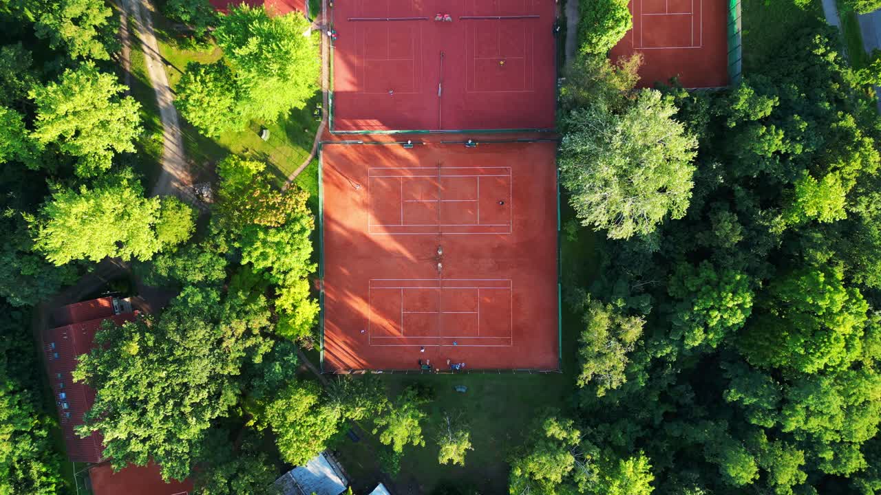 Persone che giocano una partita di tennis su campi in terra battuta durante una giornata di sole a Berlino, Germania. Telecamera drone puntata verso il basso.