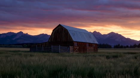 rustic barn in a field at sunset with mountains