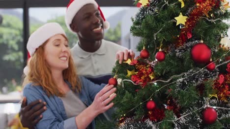 Happy-diverse-couple-wearing-santa-hats-decorating-christmas-tree