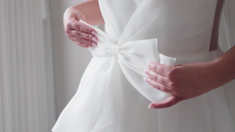 bride adjusts delicate white bow on elegant wedding dress