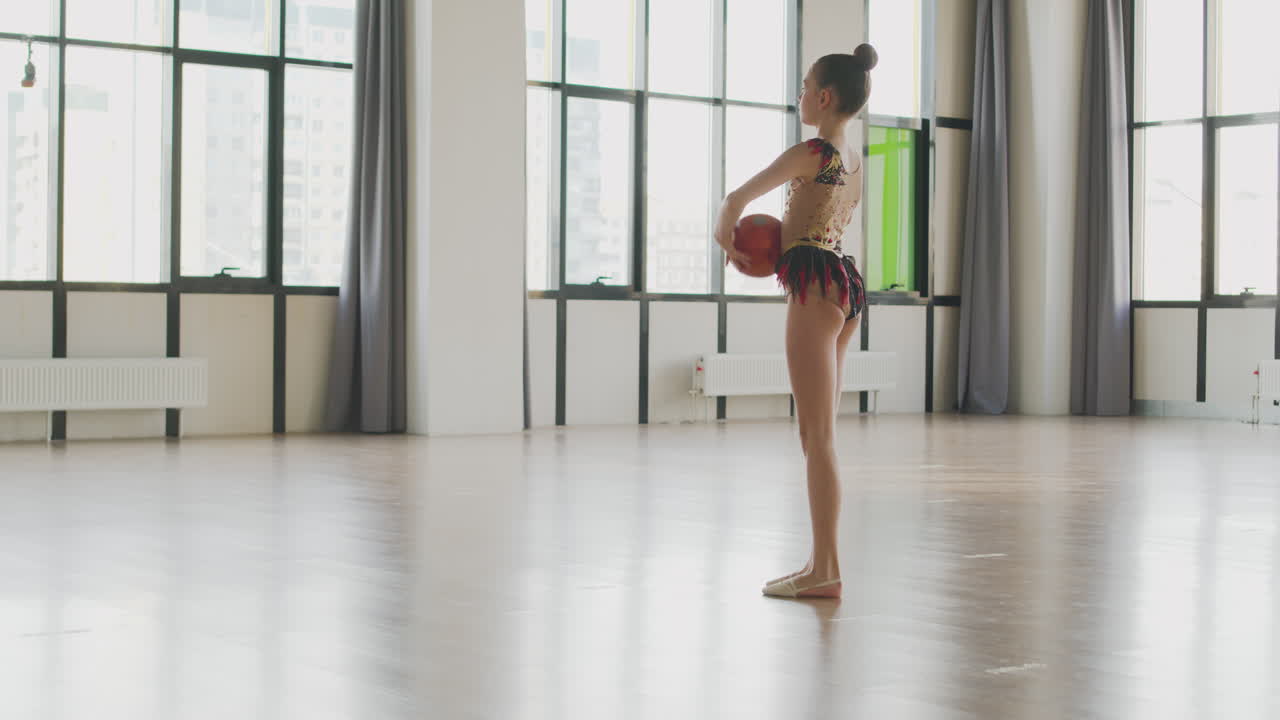 스튜디오에서 공을 가지고 리듬 체조를 연습하는 레오타드를 입은 어린 소녀