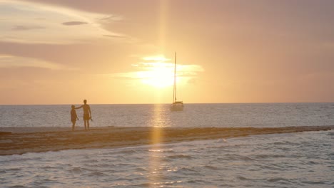 romantic couple holding hands, walking on beach and watching picturesque sunset above tropical sea and sailboat, full frame slow motion
