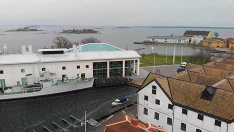 Aerial-footage-of-a-docked-Swedish-military-ship-next-to-a-museum-with-old-military-flight-hangars-in-the-background