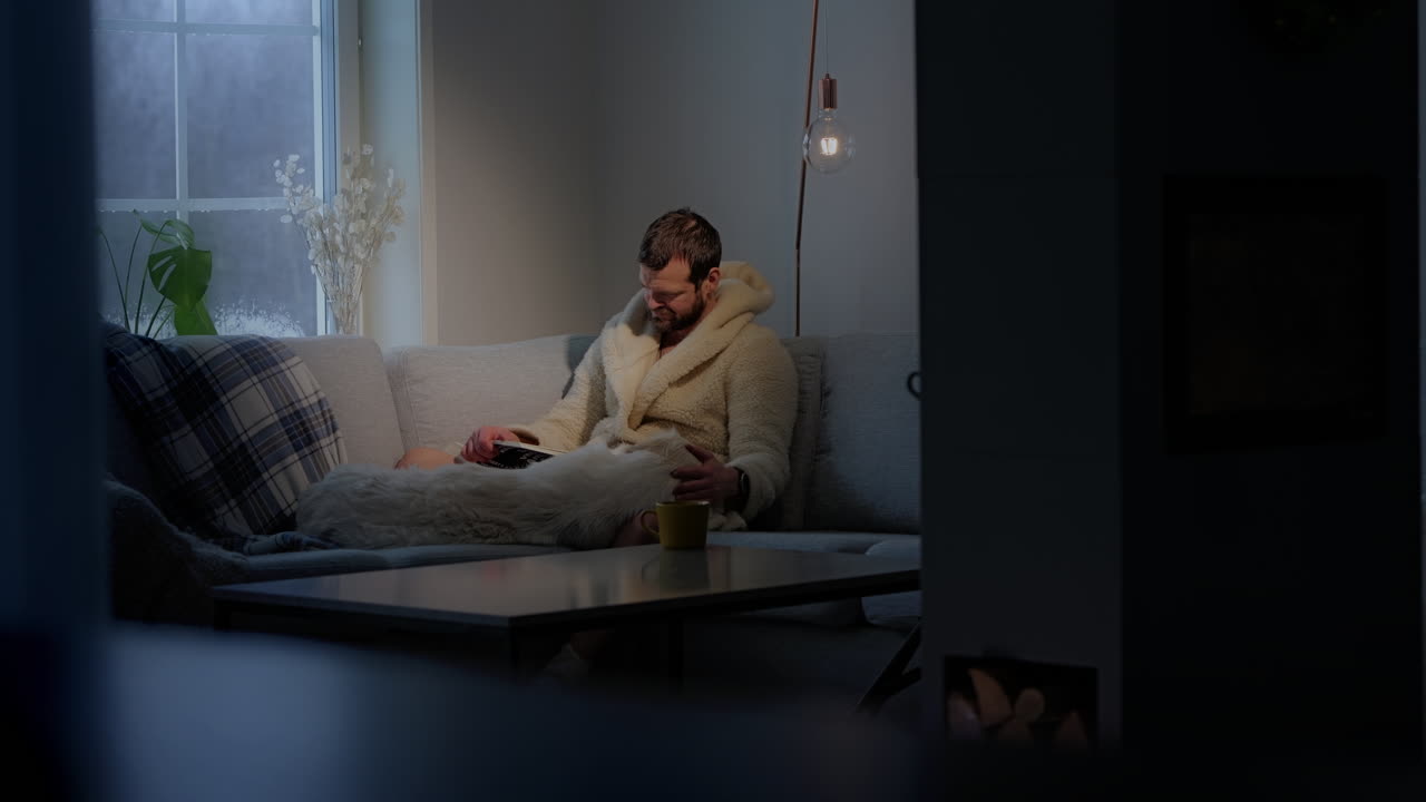 Adult man reading on sofa couch with his dog lying next to him