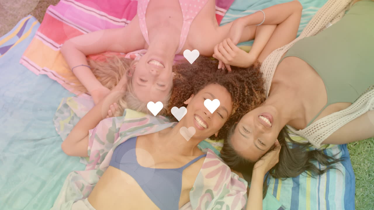 Smiling friends lying on beach towels with floating heart animation