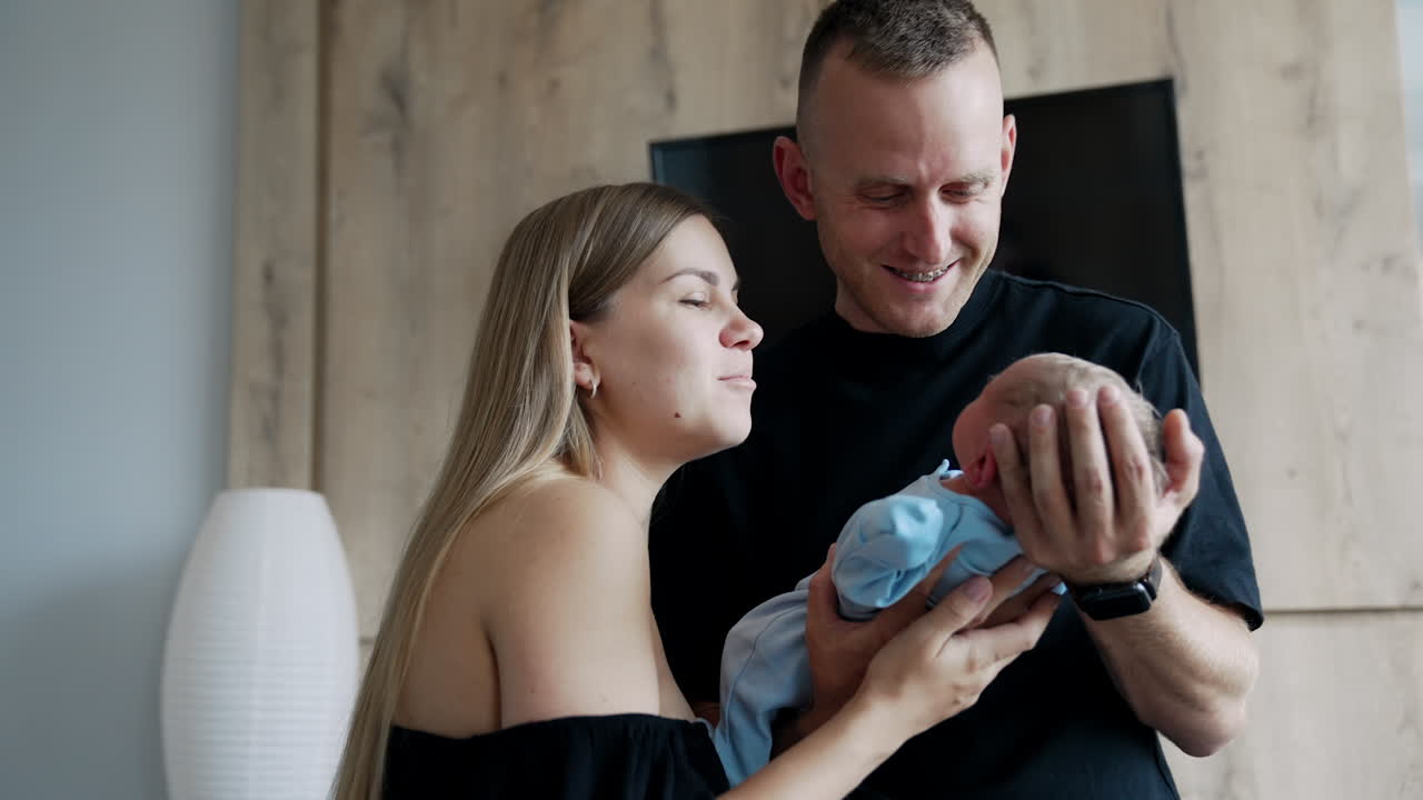 Mid-aged man holding his newborn baby carefully. Long-haired woman stands beside supporting child's back.
