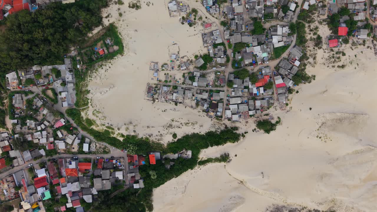 Riprese aeree con drone dall'alto che mostrano il forte contrasto tra le dune di sabbia bianca di Santinho e le colorate case residenziali di Florianópolis, Brasile.