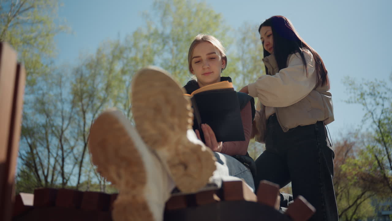 아시아인 튜터와 백인 학생이 야외에서 지식을 공유하고 있어요. 젊은 강사가 쾌적한 야외 세션에서 학생을 지도하고, 멘토는 화창한 날씨에 꽃이 피는 나무 아래에서 학생의 독서를 도와주고 있어요.