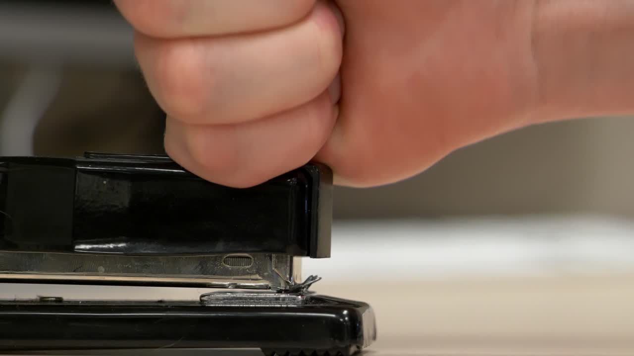 A profile view hand hitting a black stapler with no paper in it a bunch of times knocking staples out
