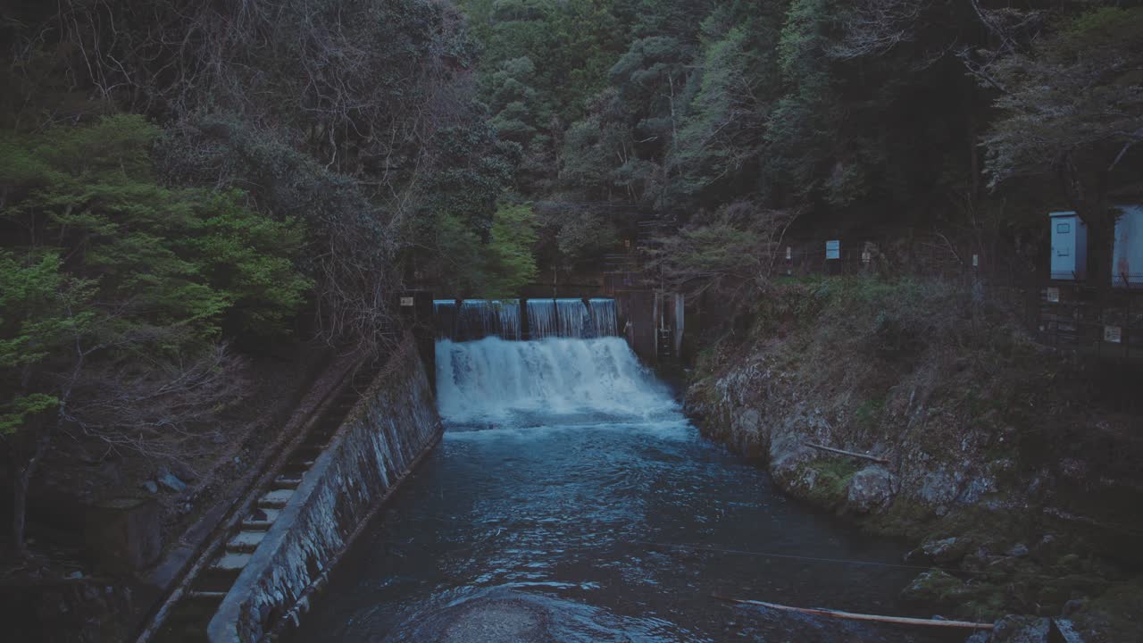 Small River In A Forest With Water Pouring Out Of Dam At Dusk - Static Shot