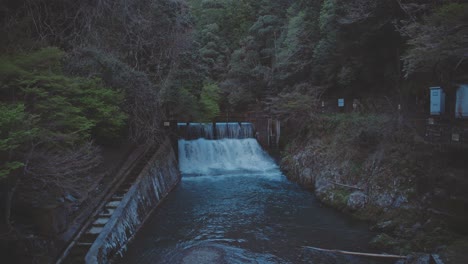 small river in a forest with water pouring out of dam at dusk - static shot