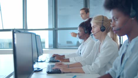 gerente de centro de llamadas masculino de pie junto a los operadores en auriculares