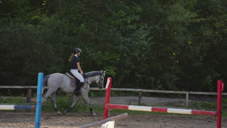 Professional-girl-rider-galloping-on-a-horse.-Girl-riding-a-horse-on-an-arena-at-sunset.-Horse-hoof-creates-a-lot-of-dust.-Competitive-rider-training-jumping.