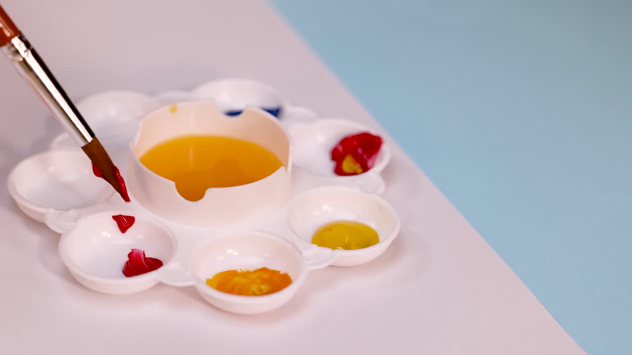 Paintbrush collects red pigment from plastic palette under soft lighting, close-up, steady camera angle