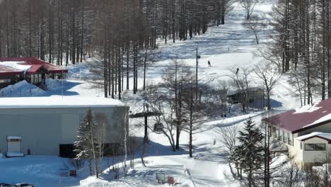 establishing shot of base of ski slopes, skiiers arriving at base of mountain where the cable car bubble cars depart from orbiting, push in telescopic shot japan ski snow run, hakuba and myoko region