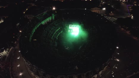 Drone-top-shot-on-the-Arenas-de-Nîmes-in-the-middle-of-the-night,-people-are-watching-the-concert-and-there-are-lights-of-several-colors