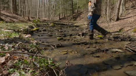 man walking in woods crossing a water way of stream