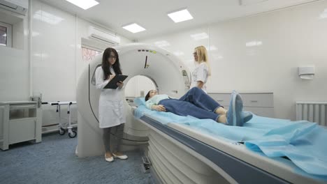 female patient is undergoing ct or mri scan under supervision of two qualified radiologists in modern medical clinic. patient lying on a ct or mri scan table, moving outside the machine