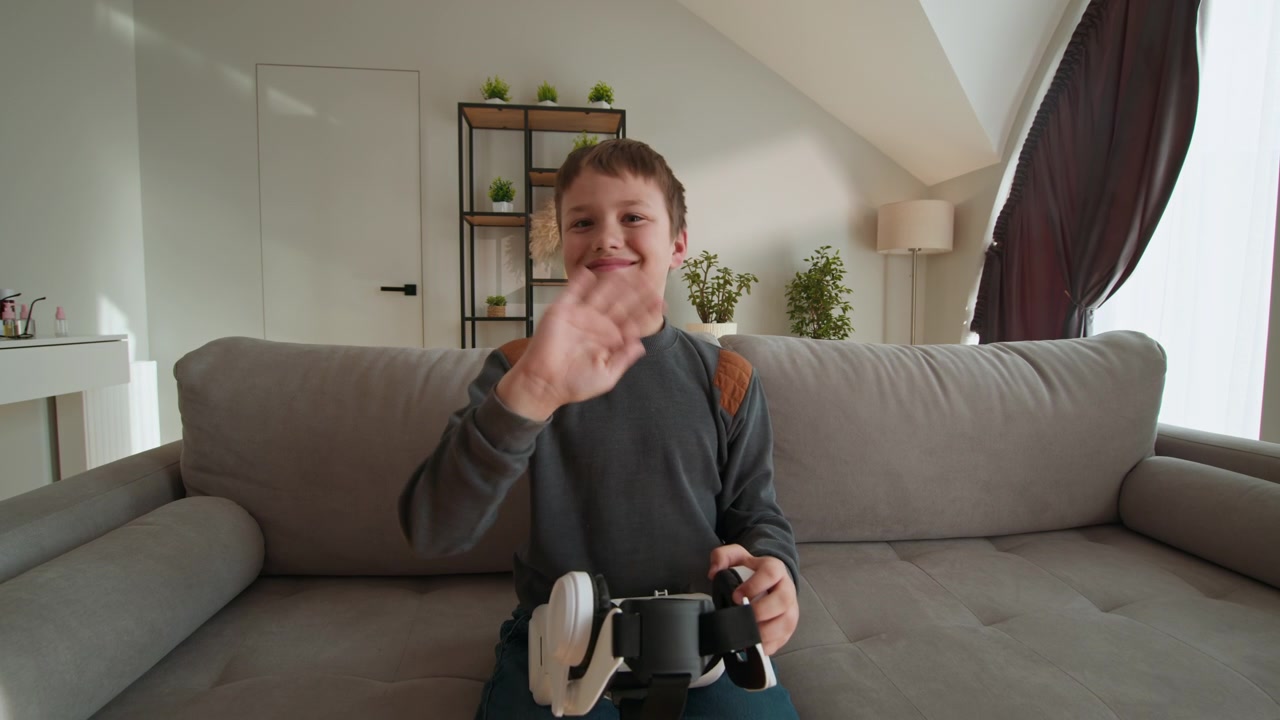 Un giovane ragazzo è seduto su un divano, con in mano un visore per la realtà virtuale, pronto per un intrattenimento immersivo.