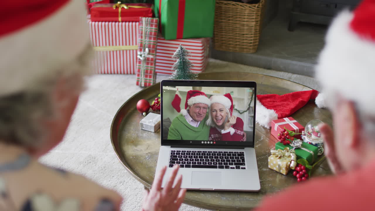 pareja caucásica de alto nivel con sombreros de santa usando una computadora portátil para una videollamada de navidad con pareja en la pantalla