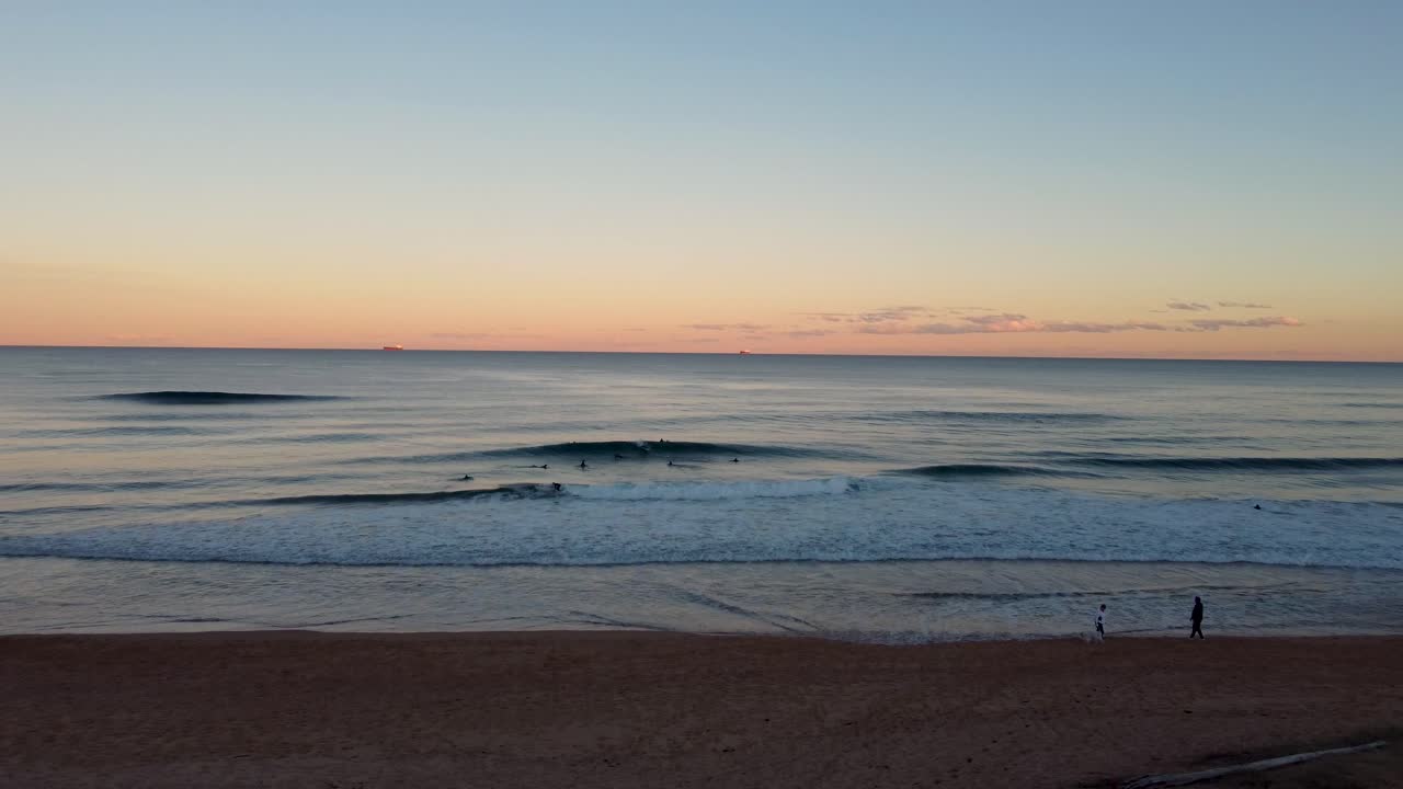 toma de drones de surfistas de la tarde con puesta de sol naranja en las olas del océano shelly beach costa central nsw australia 4k
