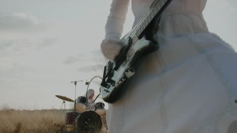 Punk-Tocando-El-Bajo-Vestido-De-Novia-Mientras-El-Baterista-Toca-De-Fondo-En-El-Desierto