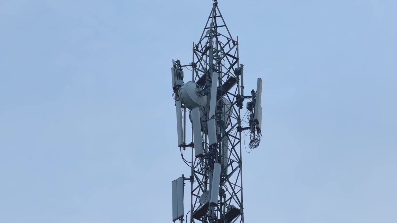 Smooth panning shot across a telecommunications cell tower showing multiple cellular antennas and communication equipment mounted on a steel lattice structure