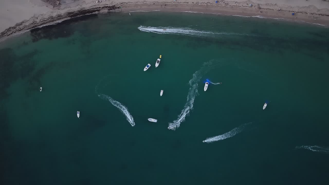 Vertical aerial shot of boats and jet skis strolling along a beach