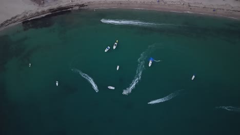 vertical aerial shot of boats and jet skis strolling along a beach