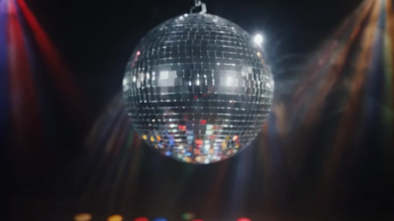 Palla da discoteca scintillante circondata da luci colorate che proiettano motivi vivaci sul pavimento, creando un'atmosfera energica per la danza e la celebrazione