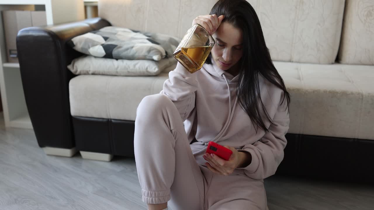 Woman with bottle of alcohol on head looking at phone, representing addiction or distress