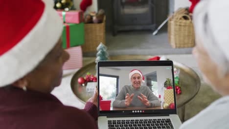 diversas amigas mayores usando una computadora portátil para una videollamada de navidad con un hombre sonriente en la pantalla