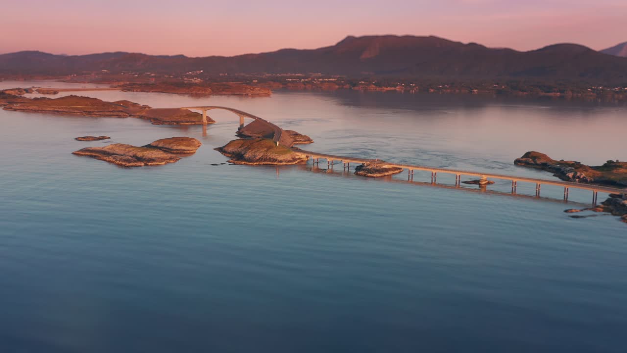 섬을 가로질러 어있는 대서양 도로의 일련의 다리의 공중 촬영, 숨막히는 일몰과 높은 산을 배경으로