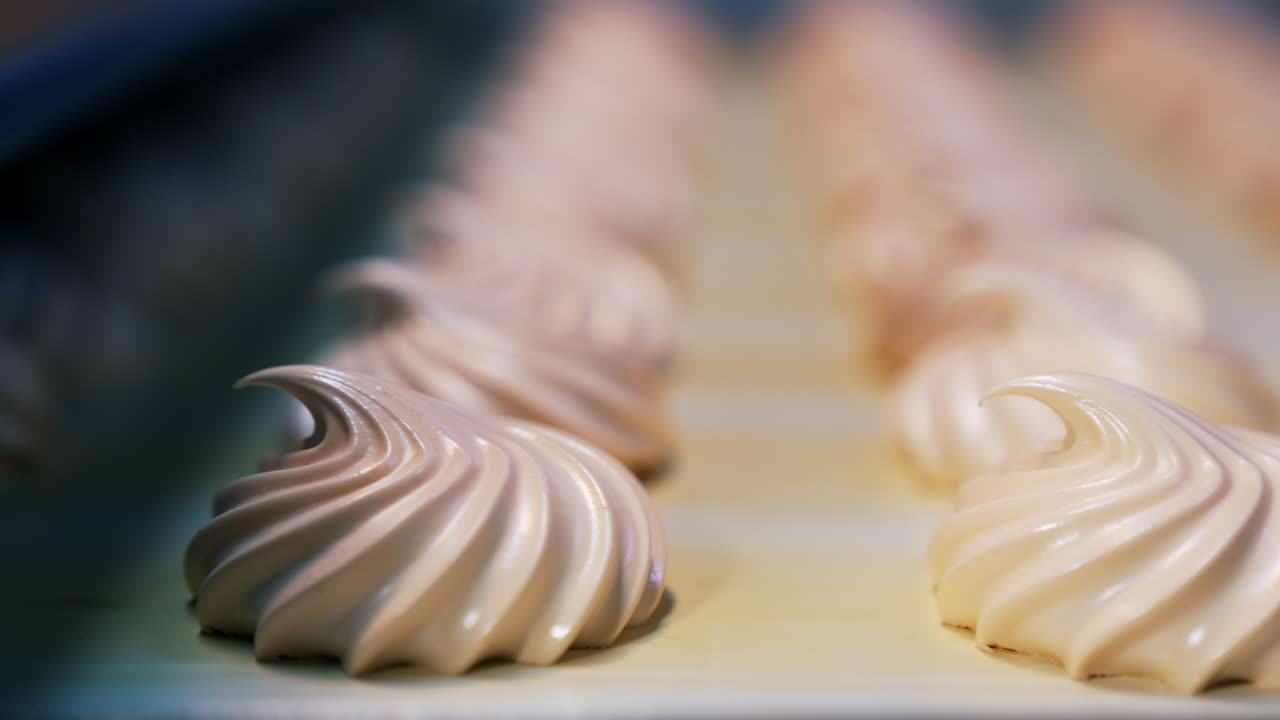Manufacturing white zephyr candies at modern confectionery factory. Creamy sweets moving along the conveyor. Close up. Blurred backdrop.